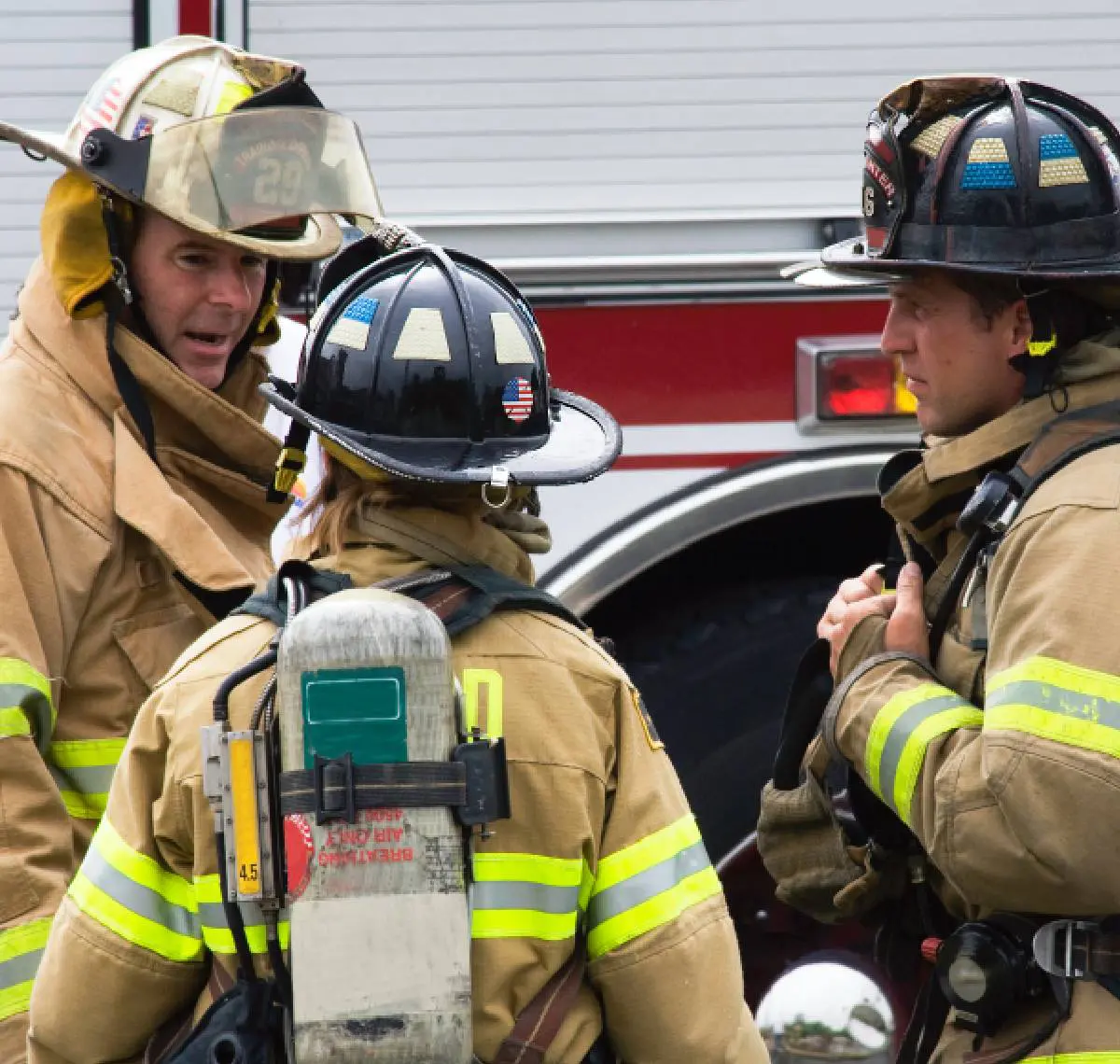 Firefighters in gear discuss next steps near a fire truck.