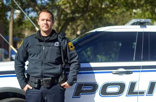 Police officer standing next to a patrol car outdoors.