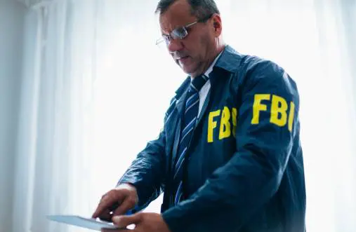 FBI agent in suit and badge working on a phone indoors.