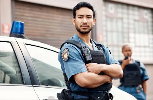 Confident police officer standing with arms crossed near patrol car.