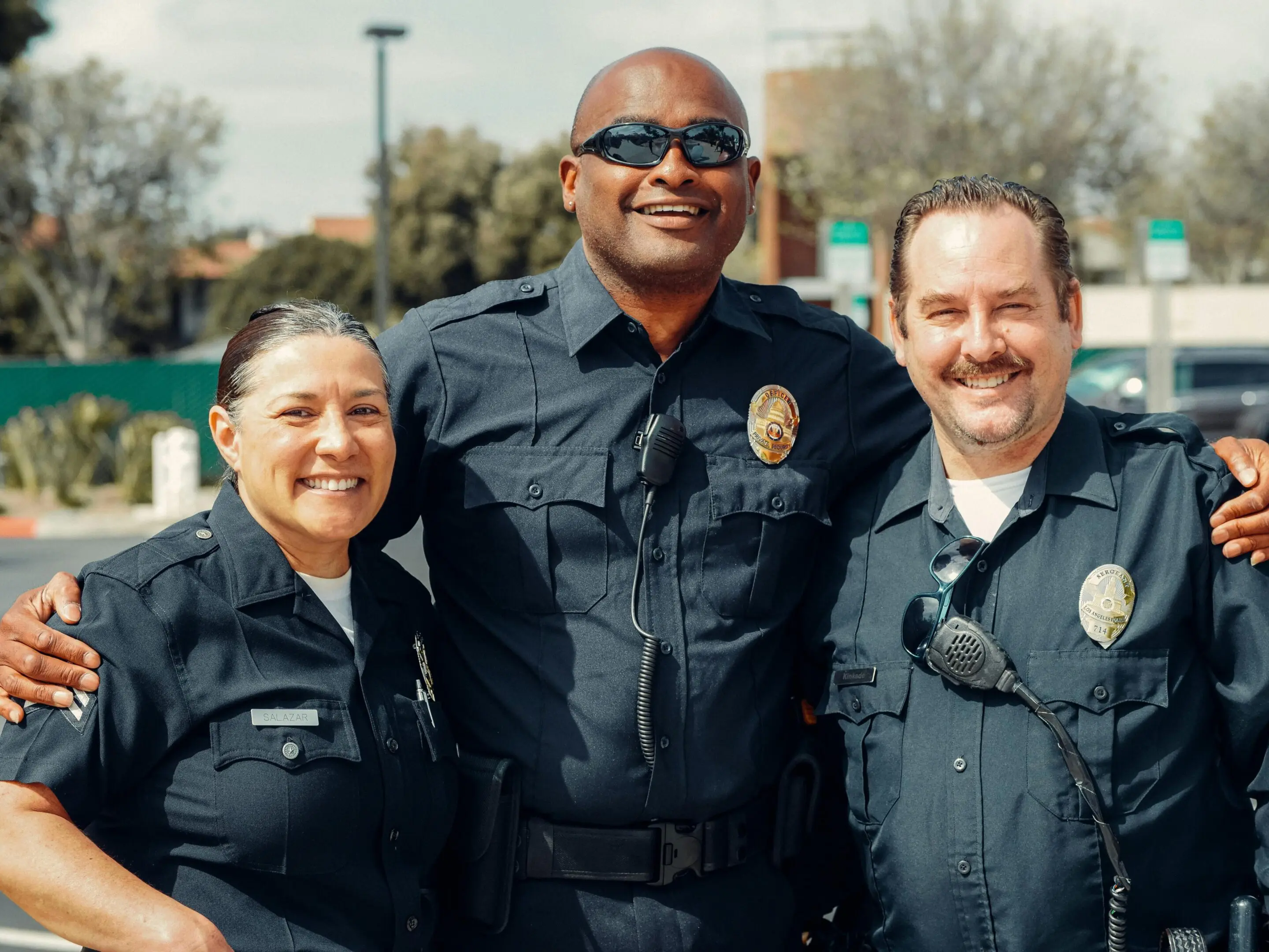 Three smiling police officers posing outdoors in uniform.